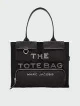 Bolso tipo tote Marc Jacobs modelo The Cargo Canvas Large Tote Bag, color tostado, confeccionado en lona con múltiples bolsillos delanteros con solapa y cierre, detalle de anilla metálica y estampado gráfico con el nombre de la marca. Cuenta con asas dobles para el hombro.