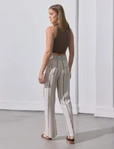 Pantalón largo de lino color beige con rayas verticales marrones. Tiene pretina ancha en punto smock con lazo ajustable, bolsillos verticales delanteros y bolsillos aplicados traseros.