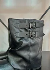Botas de caña baja color negro, con diseño holgado y dos correas decorativas con hebillas metálicas en la parte superior.