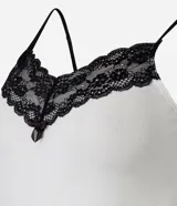 Camisón corto de color blanco, con escote en V adornado con encaje negro y tirantes finos ajustables. El ruedo también está decorado con un borde de encaje negro.