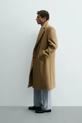 Abrigo largo color camel, de corte relajado (relaxed fit), confeccionado en tejido con mezcla de lana. Presenta cuello con solapas de muesca, manga larga, bolsillos de vivo en cadera, bolsillo interior y cierre frontal de botonadura cruzada.