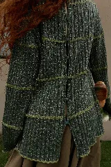 Buzo reversible de tejido fino con sutil brillo, color bordó, con cuello bote y mangas largas acampanadas. Presenta costuras decorativas horizontales y botones en forma de flor a los costados.