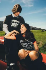 Remera tipo baby tee negra con ribetes rojos en cuello y mangas, y estampa frontal blanca con texto de marca y diseño de estilo vintage.
