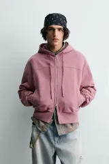 Sudadera tipo hoodie con cierre frontal de cremallera, diseño boxy fit, capucha ajustable con cordones, mangas largas con puños elásticos y bolsillos laterales. Presenta un acabado con efecto lavado.