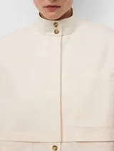 Camisa de corte recto en color crudo, con cuello chimenea y cierre frontal de botones. Presenta mangas largas con abertura y botón en los puños, canesú delantero y bolsillos de plastrón en el pecho con logo bordado. Confeccionada en una mezcla de fibras con tacto suave y acabado brillante.