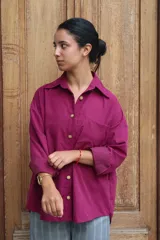 Camisa de corte oversize color fucsia, con cuello clásico, cierre frontal de botones dorados y bolsillo en el pecho.