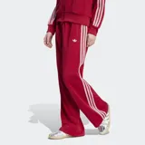 Pantalón deportivo Adidas Firebird Pinstripe color rojo con finas rayas verticales y las clásicas tres tiras blancas en los laterales. Cuenta con tiro medio, bolsillos laterales con cierre y el logo del trifolio bordado en blanco.