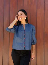 Camisa de jean azul con cuello mao, cierre frontal con botones rojos y mangas tres cuartos abullonadas con puños elásticos.