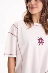 Remera blanca de algodón, corte semi boxy con mangas cortas, costuras en contraste color bordó y detalle bordado de sol en el pecho.