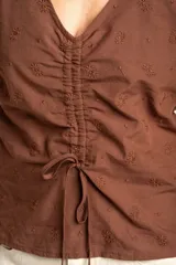 Blusa marrón de algodón con bordados sutiles, escote en V, mangas cortas abullonadas y detalle de fruncido con cordón ajustable en el centro del frente.