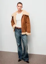 Chaqueta de efecto ante color marrón con forro y cuello de borreguito en tono crema. Presenta cierre frontal con cremallera, diseño recto y dos bolsillos laterales.