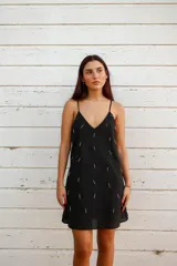 Vestido corto negro de algodón con breteles finos regulables y escote en V. Presenta bordados de canutillos y mostacillas plateadas. De corte holgado y forrado.