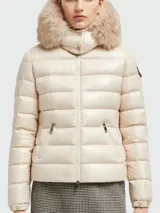 Campera puffer color crema de Moncler, modelo Badyf, con relleno de plumas, cierre frontal con cremallera, bolsillos laterales con cremallera y capucha con borde de piel sintética.