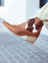 Texana de caña baja confeccionada en cuero natural, con diseño combinado en cuero liso color suela y paneles laterales con estampado de vaca. Presenta taco cuadrado de madera y punta fina.