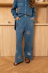 Pantalón de corte recto y fluido, color celeste, con cintura alta, trabillas para cinturón, cierre con botón y cremallera, bolsillos laterales y detalles de estrellas de strass por toda la prenda.