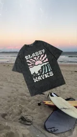 Remeron de corte holgado con efecto de lavado ácido en color negro. Presenta una estampa frontal con diseño de sol y olas en tonos pastel y la leyenda 'Classy Waves'.