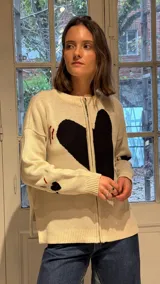 Campera tejida en hilo color crudo con diseño de corazón negro central, cierre frontal completo y detalles bordados en rojo y negro en mangas y cuerpo.