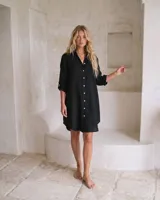 Vestido camisero de lino color negro, de corte recto y largo midi, con mangas largas abotonadas, cuello camisero y cierre frontal de botones.