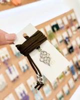 Choker de tiento de gamuza color verde oliva, con dije central de metal plateado con diseño calado y terminaciones con cuentas metálicas en los extremos.