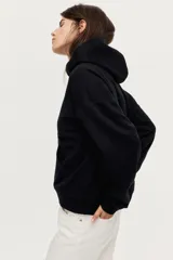 Buzo negro con capucha de doble capa, hombros caídos, bolsillo canguro frontal y puños y bajo acanalados. Interior cepillado suave.