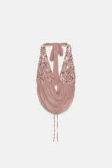 Top halter de color rosado con escote en pico pronunciado, confeccionado en tejido semitransparente con efecto arrugado y detalle de lentejuelas brillantes en la parte superior. Cuenta con tirantes para anudar al cuello y espalda descubierta con lazo ajustable.