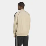 Campera deportiva Adidas Adicolor Classics de corte holgado, color beige con las icónicas tres tiras negras en las mangas y logo del trifolio bordado en el pecho. Cuenta con cierre frontal completo y puños acanalados.