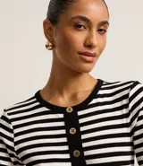 Blusa ajustada de mangas cortas, confeccionada en tejido de punto acanalado con rayas horizontales blancas y negras. Tiene cuello redondo con botones en la vista.