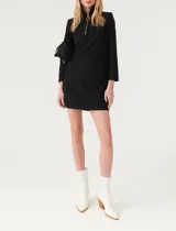 Vestido corto de corte recto, color negro, con cuello alto y cierre frontal parcial con tirador circular. Presenta mangas largas y dos bolsillos frontales de parche.