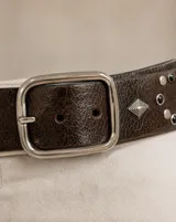 Cinto ancho de cuero marrón oscuro, con hebilla metálica rectangular plateada y apliques decorativos metálicos y piedras negras.