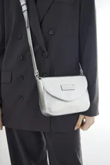 Bandolera compacta de cuero vacuno color gris con efecto gastado, solapa redondeada y correa ajustable.