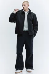 Campera rompevientos de nylon color negro, repelente al agua, con cuello elevado, cierre frontal y bolsillos laterales. Cuenta con forro de malla y puños con elástico.