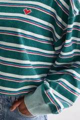 Remera cropped de manga larga y silueta oversize de algodón, con cuello redondo y diseño a rayas horizontales en tonos verdes, blancos y rojos. Cuenta con un pequeño bordado en el pecho.