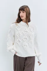 Sweater de punto grueso color rojo, con cuello alto y diseño de relieves tipo pompones en el frente y las mangas. Presenta puños y ruedo acanalados.