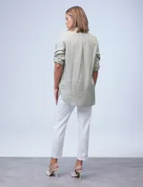 Camisa verde claro con finas líneas verticales blancas, de tencel, con cuello con solapa y abertura central con botones. Tiene dos bolsillos frontales con solapa y botón. Las mangas son largas y regulables con presilla y botón.