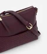 Bolso bandolera pequeño color borgoña, confeccionado en poliuretano con detalle texturizado tejido en la parte inferior. Cuenta con correa transversal ajustable, cierre de cremallera y bolsillo frontal con botón.