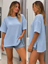 Blusa remera de bambula color celeste, con cuello redondo, mangas cortas holgadas y aberturas laterales en el dobladillo asimétrico, siendo más larga en la parte posterior.