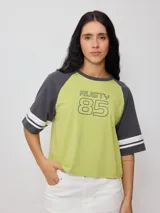 Remera bicolor Rusty con cuerpo verde lima y mangas ranglán grises con dos rayas blancas en los puños. Estampado frontal con el logo de la marca y el número 85.