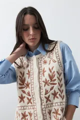Chaleco tejido color marrón con bordados artesanales de motivos florales y geométricos en color crema. Presenta cuello redondo, cierre frontal con botones y diseño sin mangas.