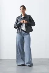 Chaqueta de cuero sintético negro con acabado brillante, cuello camisero, cierre frontal con botones a presión y bolsillos frontales con solapa.
