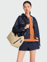 Bolso tipo crossbody de la línea Le Pliage Energy de Longchamp, en color beige. Presenta una correa ajustable y extraíble, cierre frontal con cremallera decorado con una cinta con el logo de la marca y un parche con el icónico caballo de Longchamp.