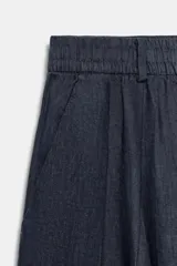 Pantalón de tiro medio confeccionado en 100% lino, color blanco, de corte amplio y recto. Cuenta con cintura elástica posterior, trabillas, pinzas en el delantero, bolsillos laterales y cierre frontal con cremallera y botón oculto.