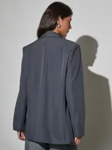 Blazer gris oscuro de corte recto y holgado, con solapas de muesca, un botón frontal y bolsillos con solapa en los laterales.