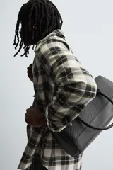 Bolso tipo bowling color negro con textura geométrica en relieve. Tiene doble asa de mano y correa de hombro ajustable y extraíble. El compartimento principal tiene cierre de cremallera y un bolsillo interior con cremallera.