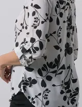 Blusa de gasa con estampado floral en tonos blanco y negro, cuello a la base con escote en V y cierre frontal parcial con botones. Presenta mangas tres cuartos con puños rectos.