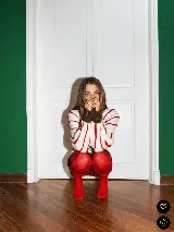 Buzo tejido a mano en lana merino, de corte oversized y diseño holgado. Presenta un fondo color crema con rayas verticales en relieve de color azul, y detalles de cuello y puños en color marrón con sutil brillo.