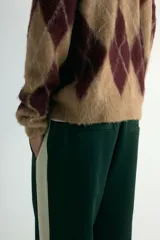 Pantalón deportivo de corte relajado en tejido efecto neopreno, color verde oscuro con franjas laterales en contraste color crema. Presenta cintura elástica con cordón ajustable, bolsillos laterales y traseros, y cierre oculto en el bajo.