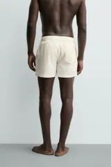 Short de baño de color beige con textura seersucker, cintura elástica con cordón ajustable, bolsillos laterales y forro interior.