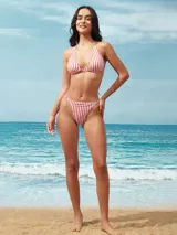 Bikini de dos piezas con estampado de rayas verticales blancas y rojas. El corpiño es de corte triangular con copas removibles y argollas metálicas doradas en los tirantes. La bombacha es de tiro medio con tiras finas ajustables en los laterales.