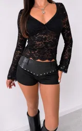 Remera de encaje negro con mangas largas y escote en V, con diseño ajustado al cuerpo y terminaciones festoneadas.