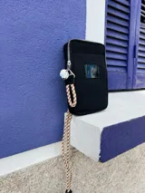 Bandolera negra de nylon con cierre superior y correa larga de cordón trenzado en tonos beige y blanco.